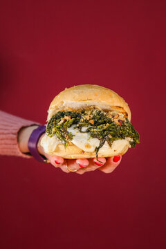 Panino riempito con hamburger di carne, friarielli napoletani, provola filante e tarallo sbriciolato appena servito in una hamburgeria e tenuto in mano da una cliente