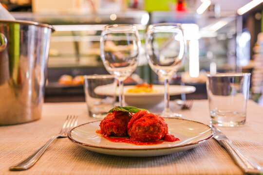 Polpette di carne al sugo condite con basilico fresco e formaggio servite in un ristorante come secondo piatto