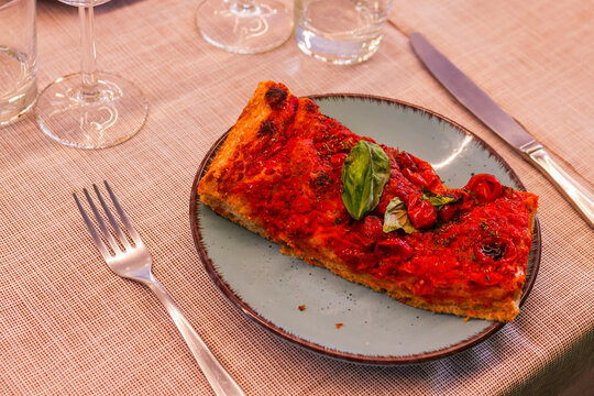 Fetta di pizza cotta in teglia con sugo di pomodoro e basilico fresco servita in una pizzeria