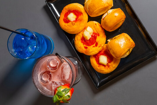 Un cocktail analcolico alla frutta e uno alcolico di colore blu serviti in un bar con pizzette e rustici come aperitivo