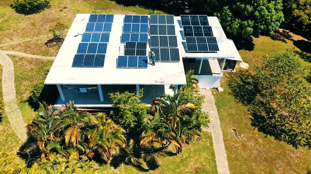 Aerial view of a worker in a safety vest cleaning rows of solar panels on a white rooftop Guanaja, Bay Islands Department, Honduras.