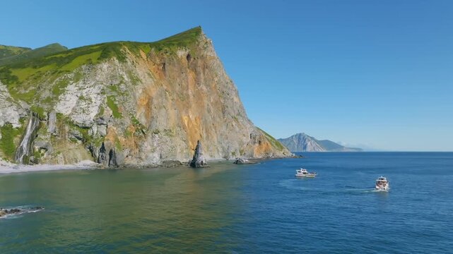 Scenic summer seascape of Avacha Bay with steep coastal cliffs, clear blue water and small tourist boats near the shore, Kamchatka Krai, Russia