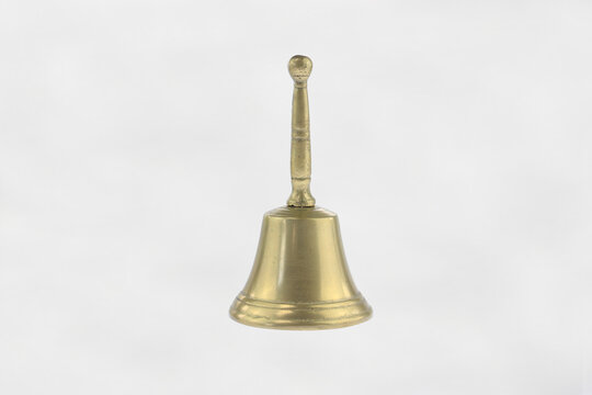 Golden bell stands alone against plain white background. Its handle curves upward, topped with a rounded knob. Bell surface gleams under soft even lighting. Vintage brass hand bell traditional  design