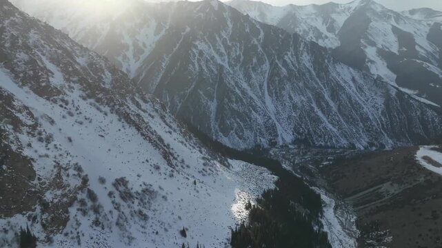Aerial footage of snow-covered Tian Shan mountains and a deep valley in Ala Archa National Park, Chuy Region, Kyrgyzstan, with soft sunrise light and winter scenery