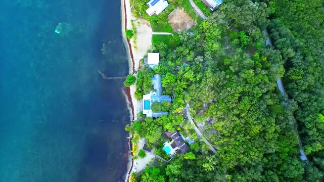 Aerial view of luxury villas with swimming pools nestled between a dense tropical forest and the turquoise Caribbean sea in Sandy Bay, Bay Islands Department, Honduras.