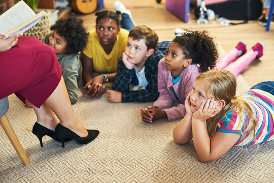 Storytelling, teacher and students on carpet, education and listening with child development. Woman, group or kids in school, relax or help with language growth, fantasy or learning with reading book