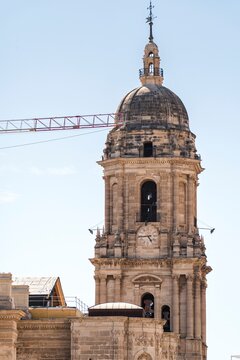 Work on the roof of Malaga Cathedral, installing new tiles on a wooden structure, with a crane passing in front of its iconic single tower