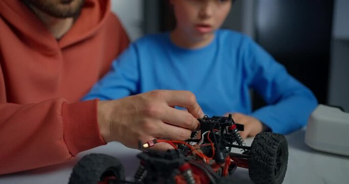 Father and son assembling a remote controlled toy car at a table, learning electronics, wiring, and mechanical skills through hands-on teamwork