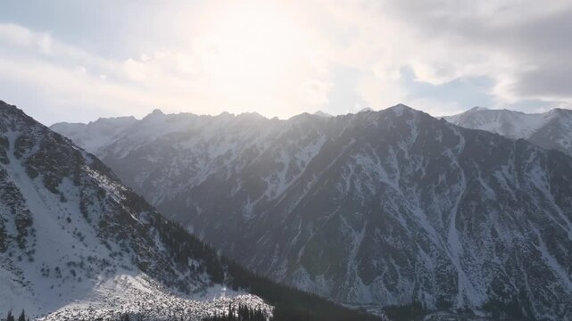 Aerial footage of snow-covered peaks and rugged ridgelines above a conifer forest in Ala Archa National Park, Chuy Region, Kyrgyzstan, in soft winter light