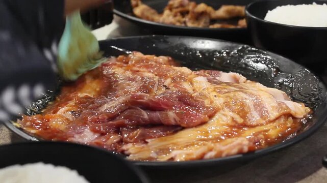 Close up of hand marinating raw beef slices with brush for Korean BBQ.