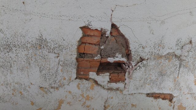 Peeling cement on white wall exposing red bricks, damaged plaster texture construction defect urban decay detail