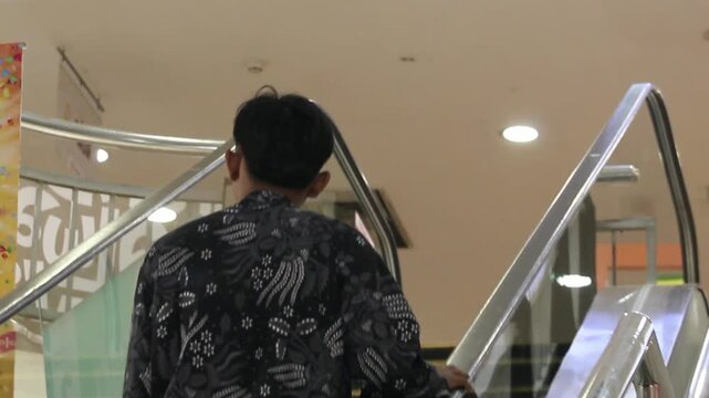 A man going up an escalator inside a shopping mall.