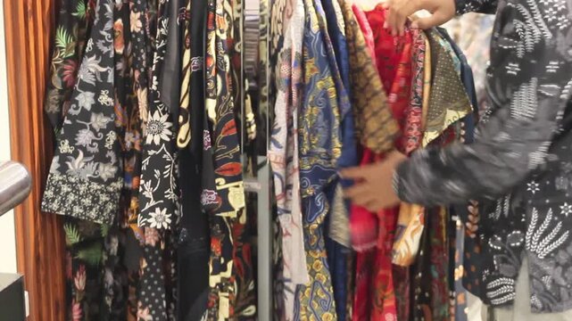 Close up of hand choosing traditional Batik shirts on a clothing rack.