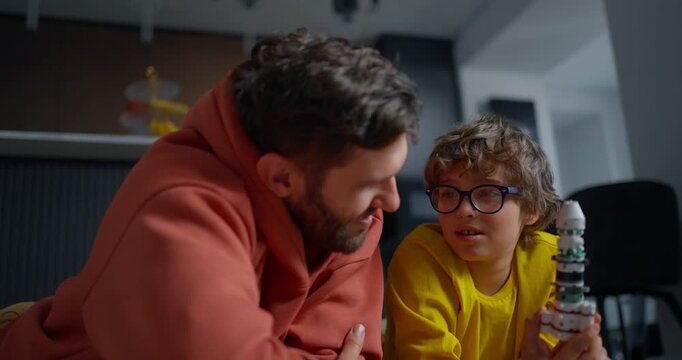 Father and young son spend quality time indoors examining a handmade toy rocket model together, sharing curiosity, learning, and playful bonding at home