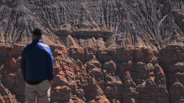 Traveler stands at the edge of Ubehebe Crater in Death Valley National Park gazing at dramatic volcanic rock formations with colorful layered sediment walls and rugged desert terrain.