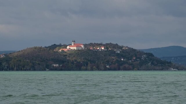 The famous Benedictine monastery on the Tihany peninsula on a sunny autumn day. Ducks flying over the wavy green water of Lake Balaton in the foreground. Scenic landscape in Hungary.