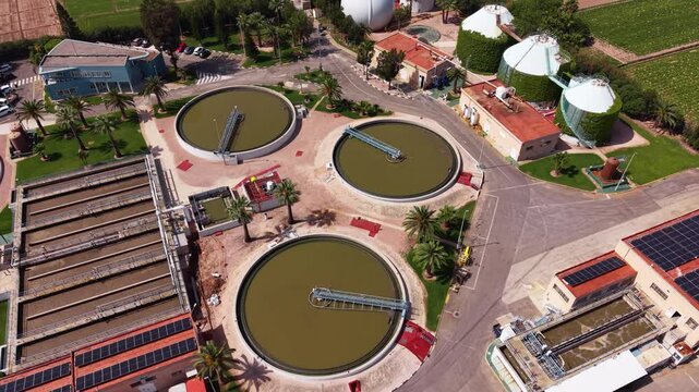 Modern wastewater treatment plant in Spain featuring circular clarifier tanks, biological treatment basins, biogas storage dome, and solar panels viewed from above