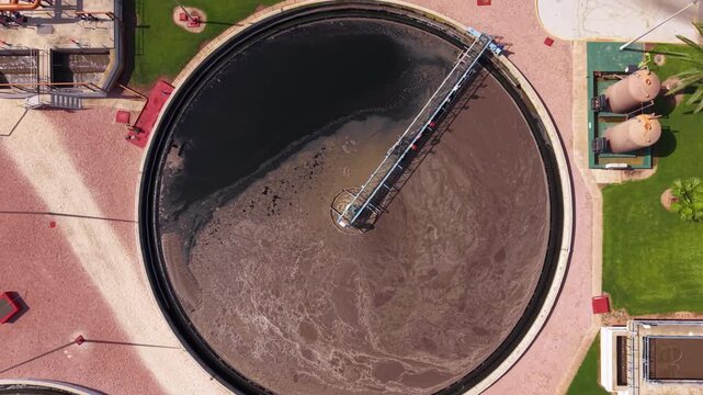 Overhead view of a circular clarifier tank at a wastewater treatment plant in Spain, showing sedimentation process with rotating mechanism and surrounding facility infrastructure