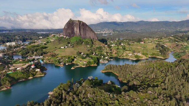 A cinematic drone trucking rotation (orbit) showing the iconic Piedra del Pe&ntilde;ol surrounded by blue turquoise lakes and lush green Andean mountains in Guatap&eacute;, Antioquia, Colombia.