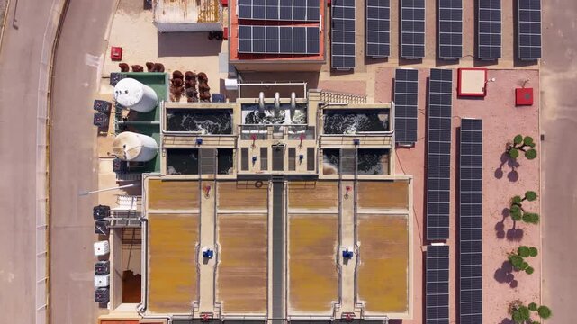 Modern wastewater treatment plant with biological nitrogen and phosphorus removal, aeration basins, secondary clarifiers, solar panels and green landscaping viewed from above