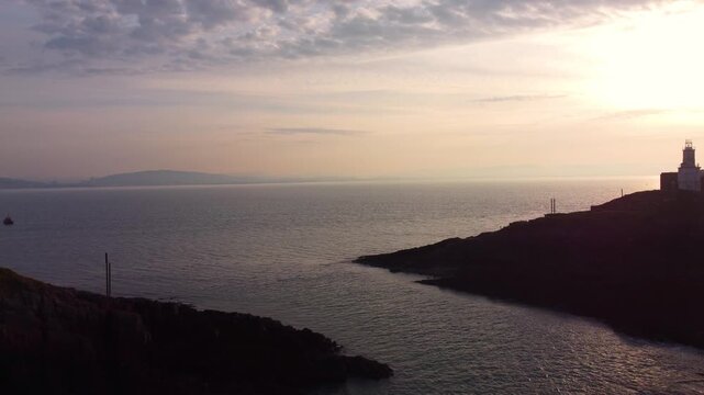 Dramatic Sunrise Aerial of Mumbles Lighthouse on Island at Sunrise. Soft Golden Hour Lighting with Welsh Coastline in Background. Perfect for tourism, travel documentaries. Wales, UK. 4K.