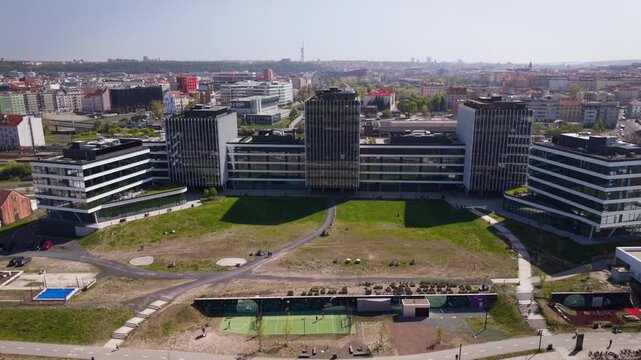 Cinematic aerial view of modern office buildings and Holesovice train station area with Prague city skyline and Zizkov Tower on a sunny day