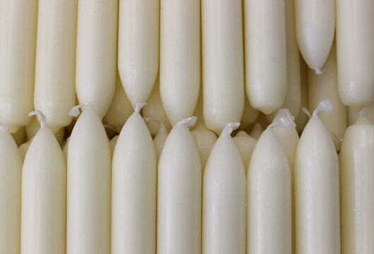 Identical paraffin candles with white protruding wicks are laid out in order
