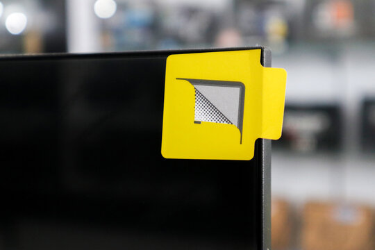 Close up of a yellow pull tab sticker on the corner of a black monitor screen for peeling off protective film.