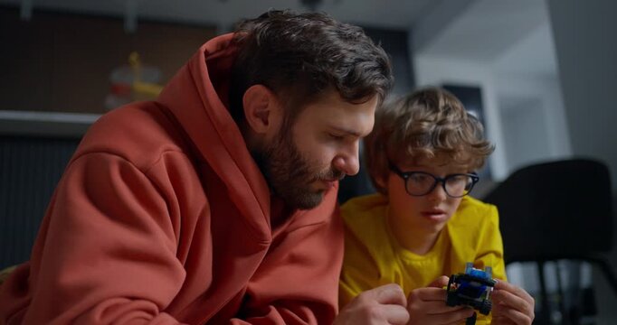 Father and young son concentrate together while assembling a small electronic toy, sharing a quiet learning moment at home