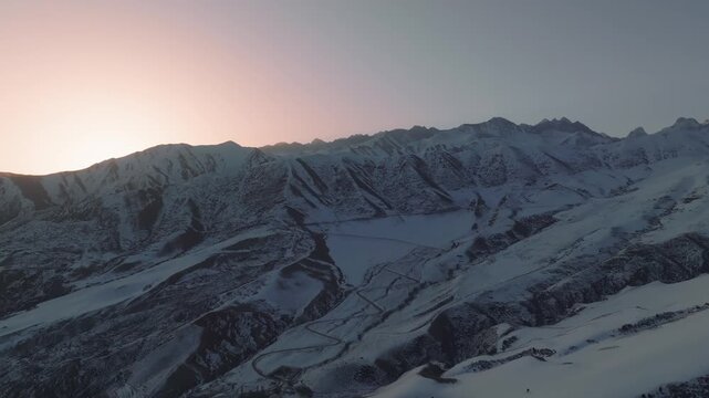 Drone footage of snow-covered ridges and winding mountain road in Chunkurchak Valley, Chuy Region, Kyrgyzstan at sunrise, serene winter landscape
