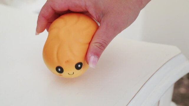 hand firmly squeezing soft yellow kawaii squishy dumpling toy with cute smiley face and rosy cheeks on white table surface close-up