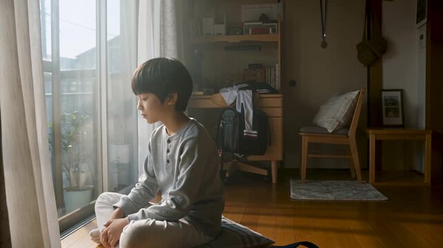 自宅の窓際で一人佇む不登校の小学生男子（孤独、悩み、家庭学習）