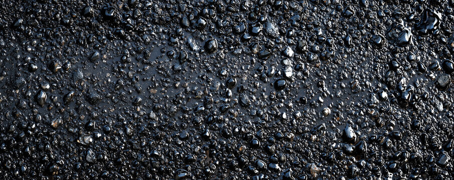 wet dark asphalt road surface with water reflections and rich stone aggregate texture