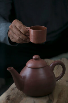 Person holding a small cly cup over s teapot