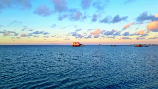 Aerial view of a coastal building on the water under a sunset sky with soft clouds in Sandy Bay, Bay Islands Department, Honduras.