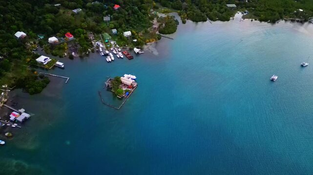 Aerial view of Sandy Bay with turquoise water, lush green hills, and boats docked along the shoreline in Sandy Bay, Bay Islands Department, Honduras.