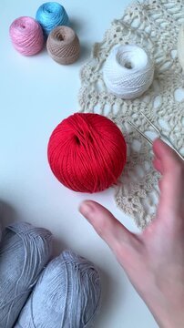 A woman's hand gently places a ball of thread on a white table. A cozy hobby at home. Tangles, hooks, crocheting. A sense of order and inner balance, the pleasure of simple, understandable actions