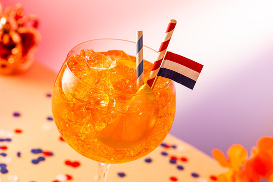 Aperol spritz cocktail served in a glass with ice and a small Dutch flag, surrounded by festive decorations for Kings Day celebration