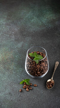 A glass filled with roasted coffee beans and fresh mint leaves, placed on a textured dark surface, creating a rich visual contrast, stories templates with copy space
