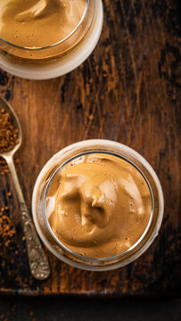 Whipped Dalgona coffee dessert displayed in glass jars on a rustic wooden table, accompanied by a spoon and coffee grounds, showcasing delicious texture, stories templates with copy space