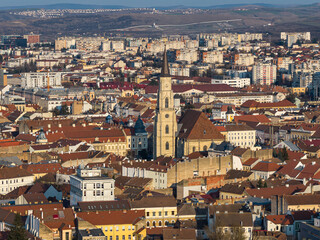 Obraz premium Aerial landscape of the historical center of Cluj-Napoca, Romania, showing the red-tiled roofs, the tall spire of St. Michael's Church, and surrounding hill. Cluj-Napoca, travel to Transylvania.