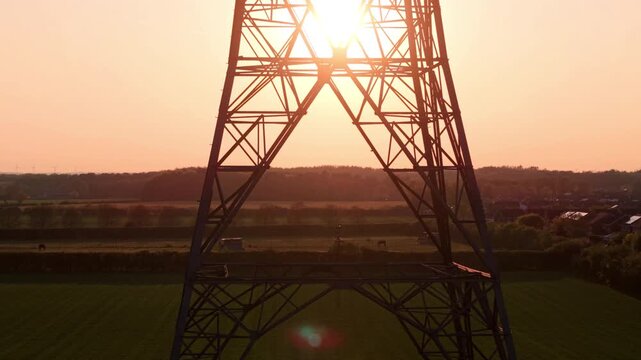 Aerial view of an electricity pylon at sunset with sun flare over green fields in Armthorpe, Doncaster, England, United Kingdom.