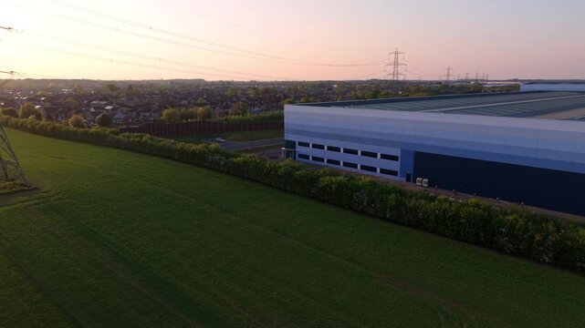 Aerial view of a large modern warehouse building next to green fields and power lines during sunset in Armthorpe, Doncaster, England, United Kingdom.