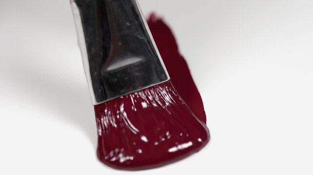 Macro video of flat paintbrush applying thick glossy dark red paint stroke on clean white background with copy space, concept of creative painting process