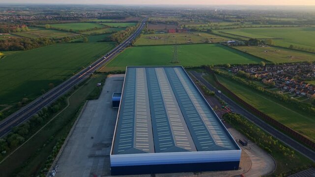 Aerial view of a large industrial warehouse building next to a highway and green fields during sunset in Armthorpe, Doncaster, England, United Kingdom.