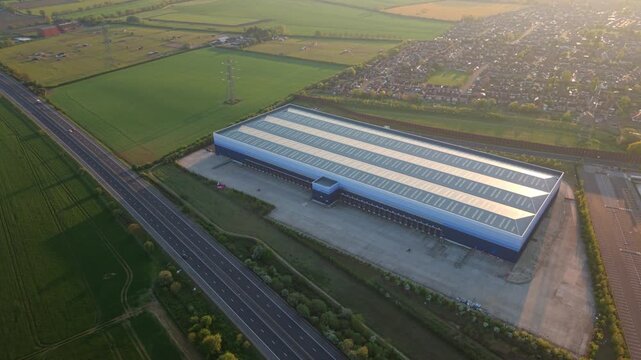 Aerial view of a large industrial warehouse and distribution center next to a highway during golden hour in Doncaster, England, United Kingdom.