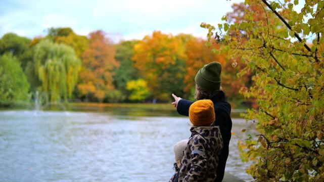 Young family with a father and two children enjoying a scenic view of a lake in a park during a beautiful autumn day, with the parent pointing at something interesting in the distance