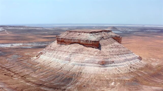 Aerial drone flies forward above Bozzhyra landscape in Mangistau Kazakhstan revealing isolated chalk mesa with layered limestone cliffs, vast desert plateau and dramatic geological formations