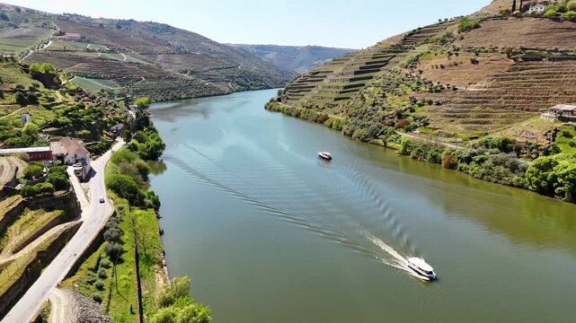 Aerial view of boats cruising on the Douro River surrounded by terraced vineyards and lush green hills in Pinhao, Vila Real, Portugal.