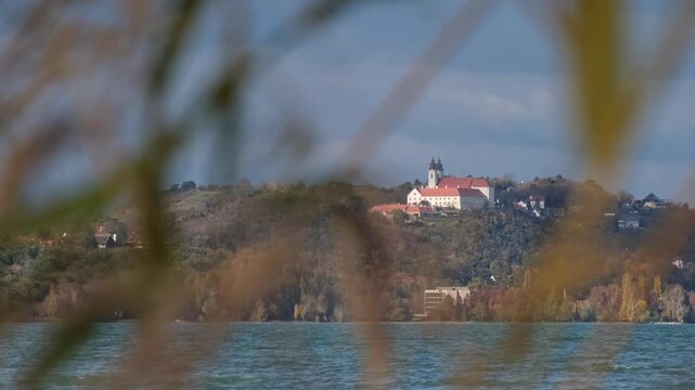 Close-up of the famous Benedictine monastery on the Tihany peninsula on a sunny autumn afternoon. Out of focus reeds and wavy water of Lake Balaton in the foreground. Slow motion landscape in Hungary.